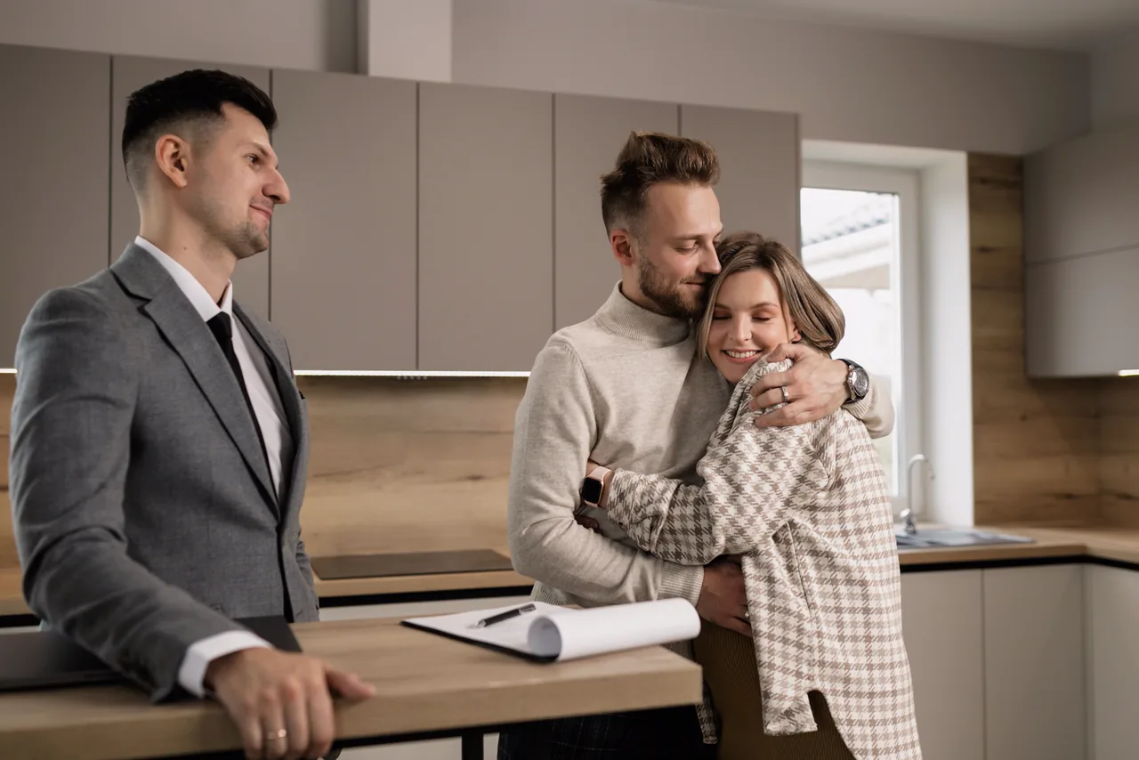 A couple hugging in their new kitchen beside their real estate agent